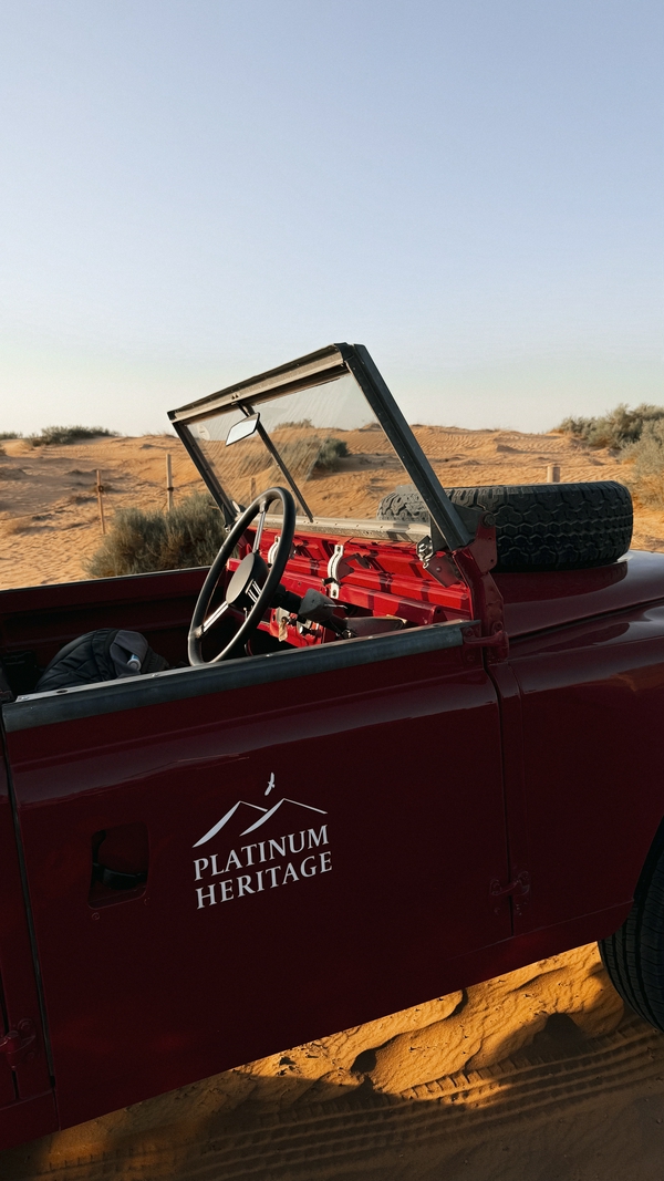 Vintage Land Rover in a vast desert landscape during sunset.