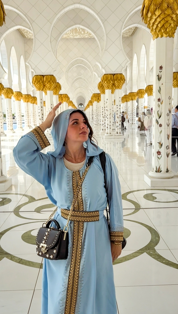 A woman in traditional attire at the Sheikh Zayed Grand Mosque, showcasing its architectural beauty.