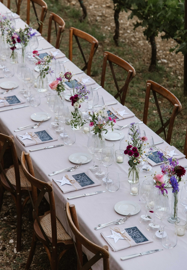 Outdoor dining table elegantly set with flowers and chairs.