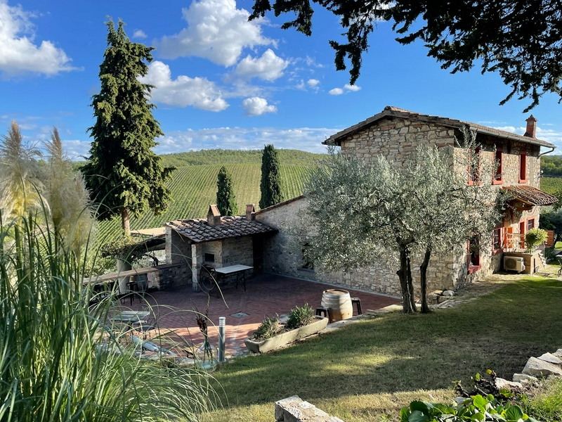 Traditional Tuscan house with trees and vineyard under a clear sky.
