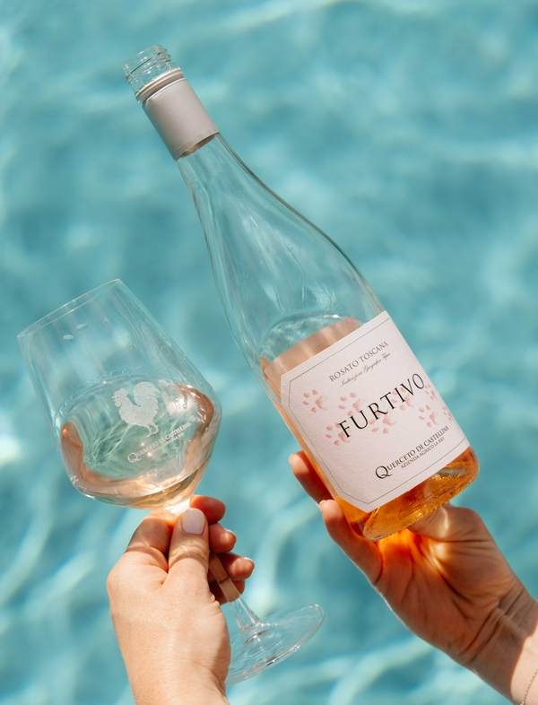 Wine bottle and glass by a pool, showcasing leisure at Querceto di Castellina.