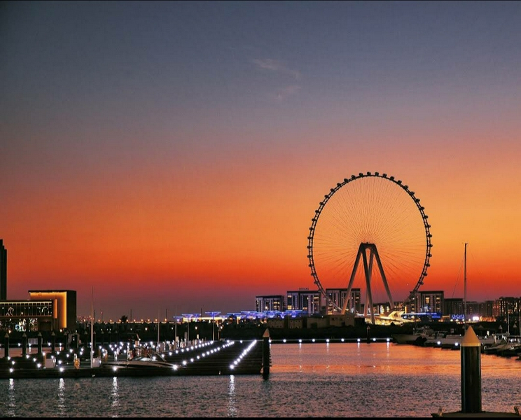 Ferris wheel at Dubai Marina with sunset and city lights.