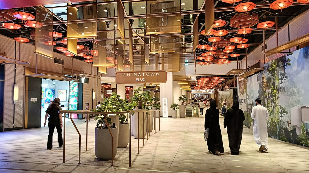 Indoor shopping mall in Chinatown Dubai with people, plants, and lanterns.