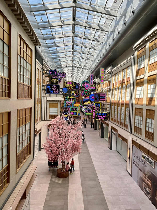 Indoor shopping mall with glass ceiling and people socializing.