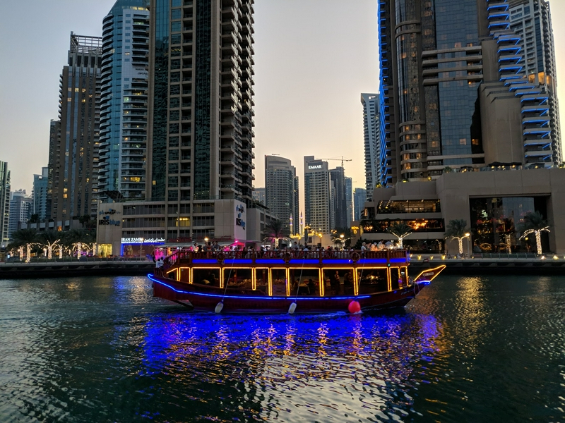 A boat navigating the waters of Dubai Marina with a stunning cityscape in the evening.