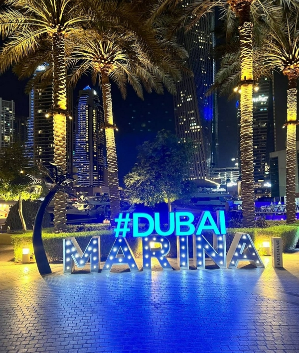 Dubai Marina at night showcasing palm trees, city lights, and neon signs.