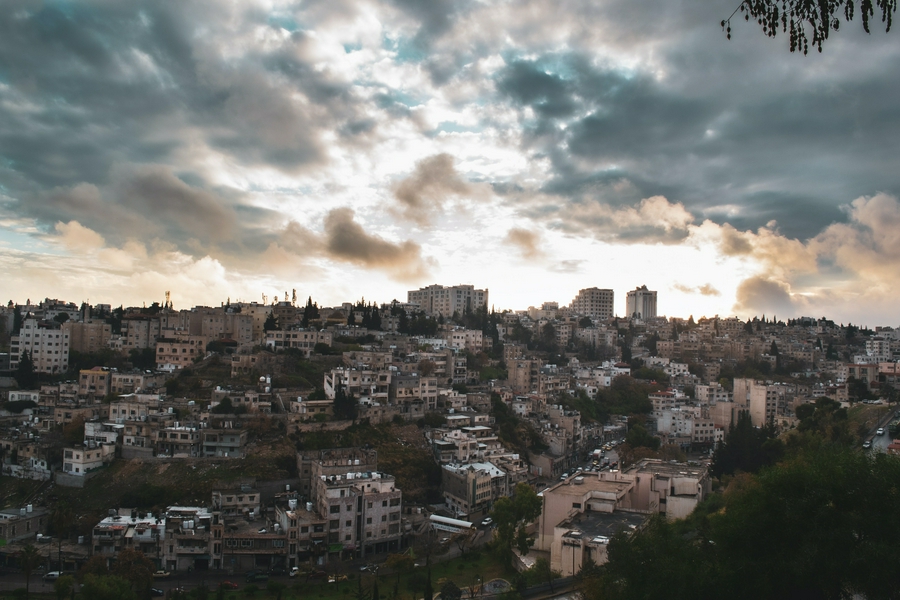 Cityscape of Amman showcasing modern and traditional architecture under a cloudy sky.