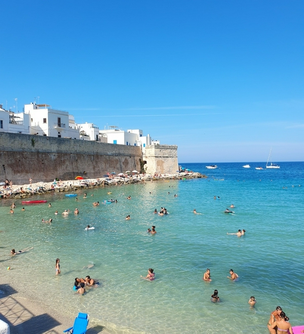 Golden sandy beach in Monopoli with clear blue waters and historic architecture.