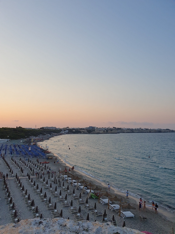 A beautiful beach at sunset with colorful umbrellas and people enjoying the scenery.
