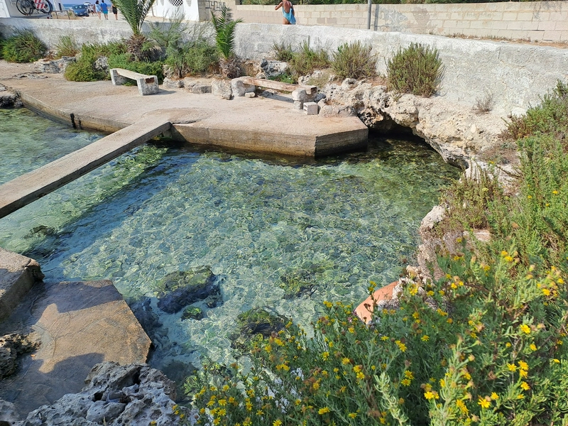 Beautiful Torre Lapillo Beach featuring inviting water, rocks, and lush coastal plants.