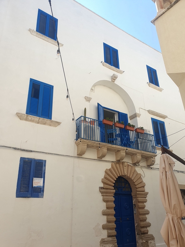 A prominent building in Otranto showcasing intricate architectural details and balconies surrounded by plants.