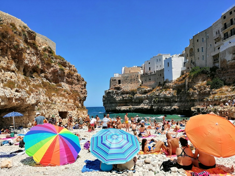Vibrant beach scene with golden sands, colorful umbrellas, and dramatic cliffs.