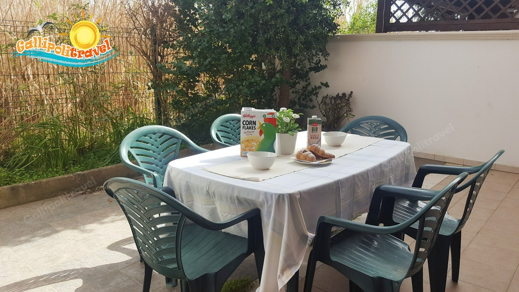 Outdoor dining table with chairs set for breakfast surrounded by plants.