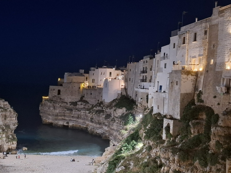 Night scene showcasing vibrant buildings, cliffs, and a beach beside the sea.