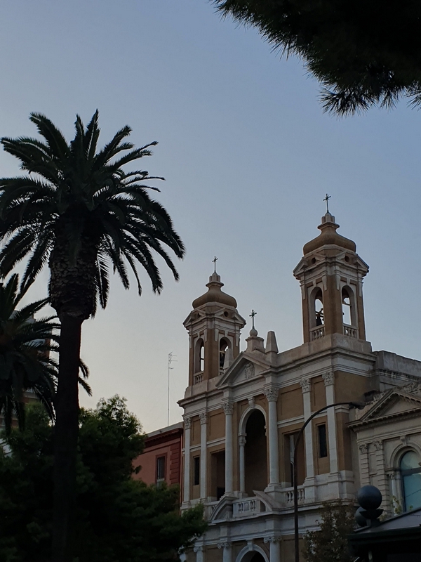 Intricate church design and palm trees under a vibrant sky in Taranto.