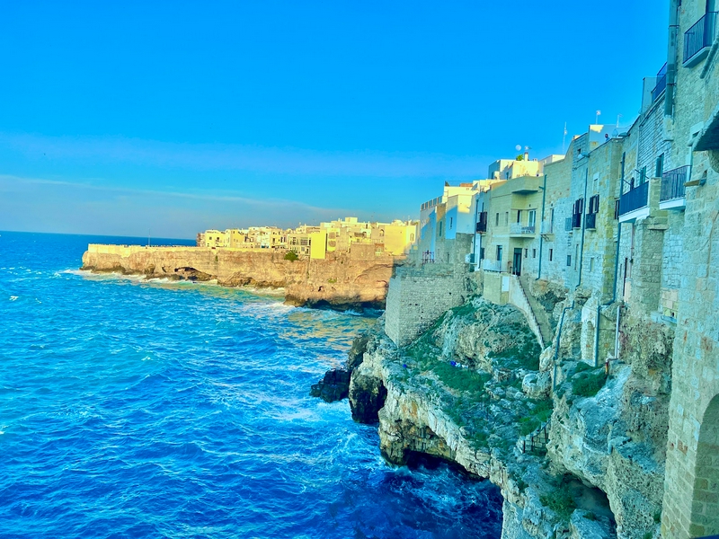 Dramatic cliffs rise above the ocean under a clear sky.