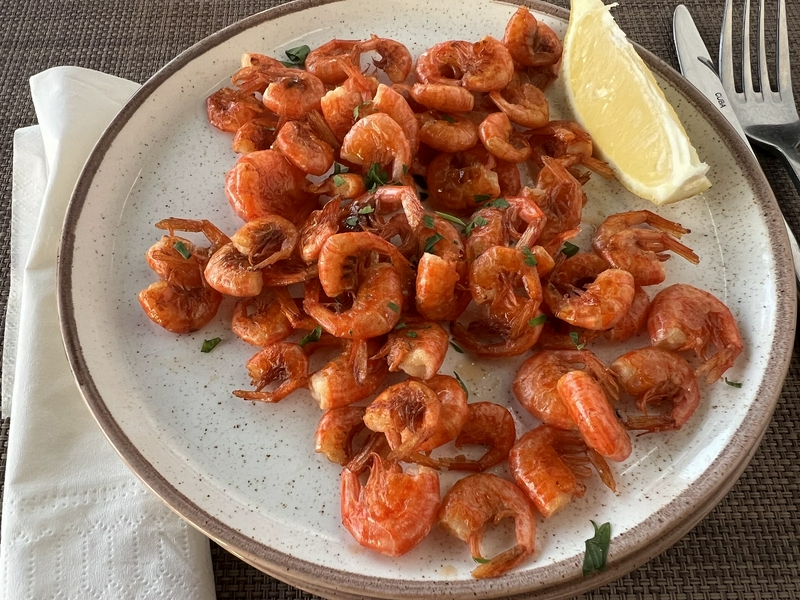 A plate of shrimp garnished with lemon, fork and napkin beside it.