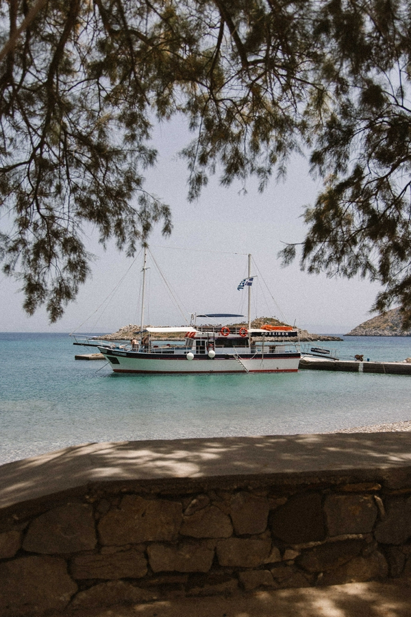 A picturesque view of Symi featuring a boat by the shore, surrounded by lush trees and the Aegean Sea.