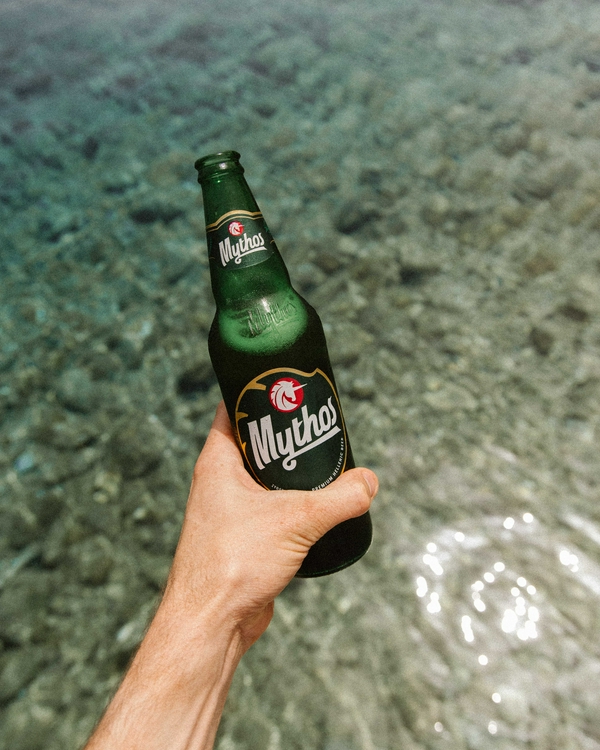 A hand holding a bottle of beverage near the serene waters of Symi.