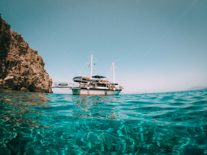 A boat on the Aegean Sea near Symi, surrounded by rocks and a clear sky.